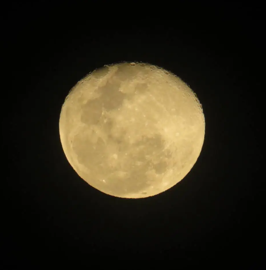 A golden close-up of the moon showing craters and lunar seas